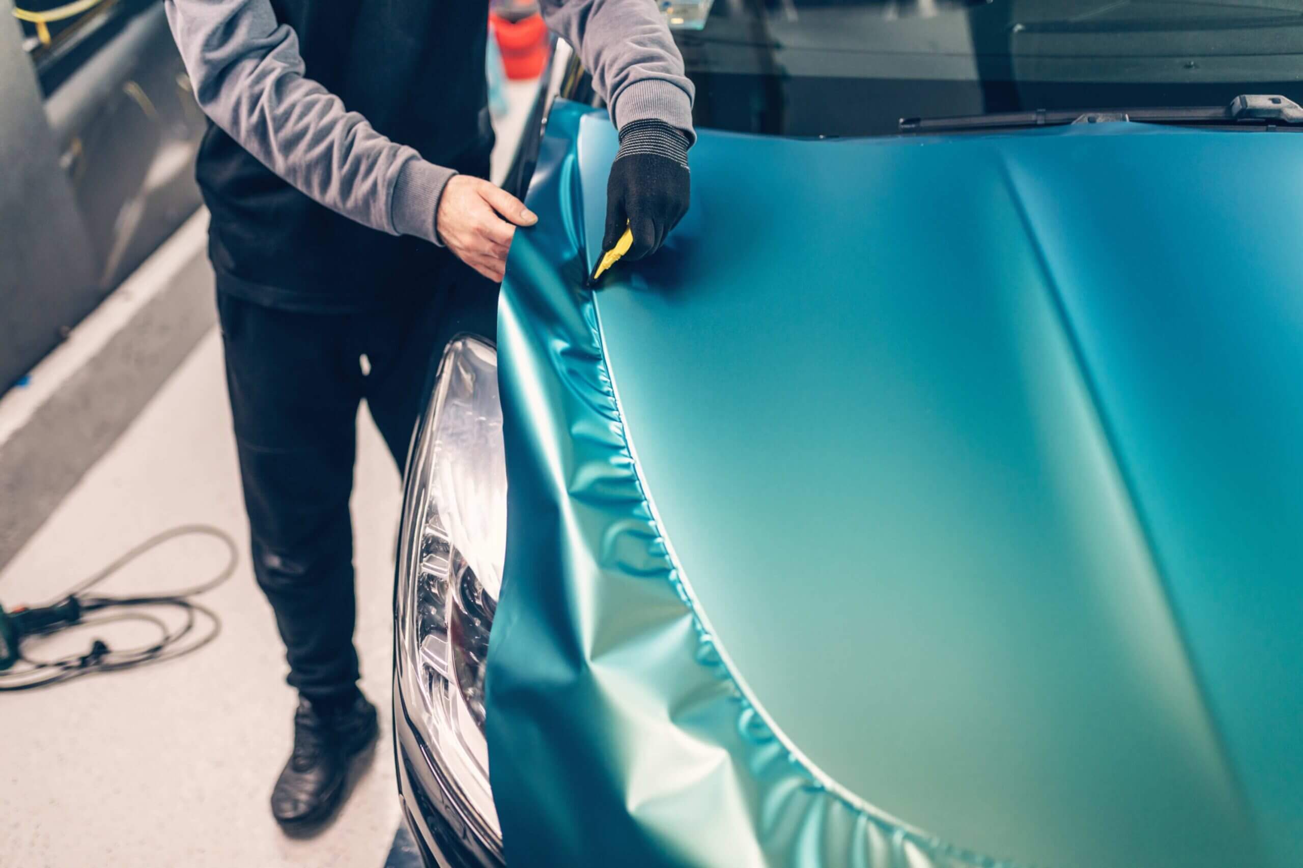 Person applying vinyl wrap to car hood.